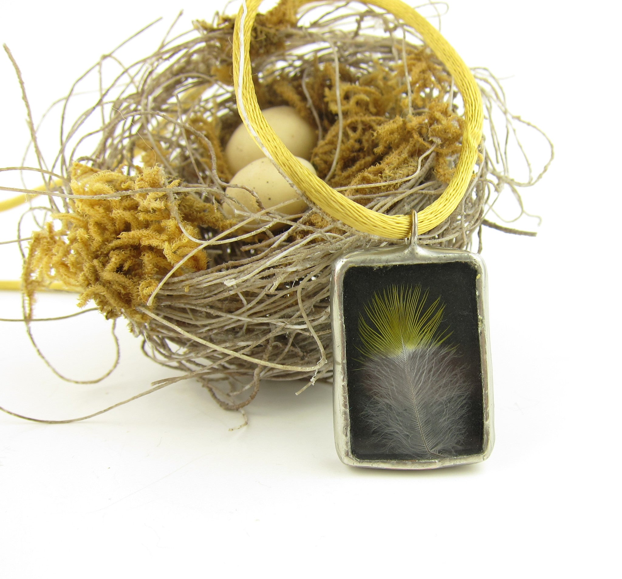 A real bird feather is sandwiched between glass salvaged from a broken window in this soldered pendant necklace.